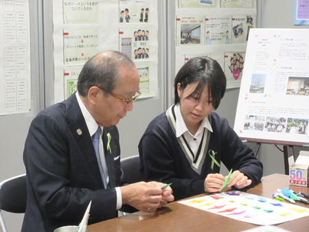折り鶴作成の体験コーナーで松井市長に説明する高校生